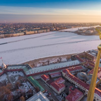 Aerial view of golden Angel and Cross on spike of the Peter and Paul cathedral in Saint Petersburg at sunset, frozen Neva River, sunny frosty day, Winter Palace, Admiralty, Rostral columns