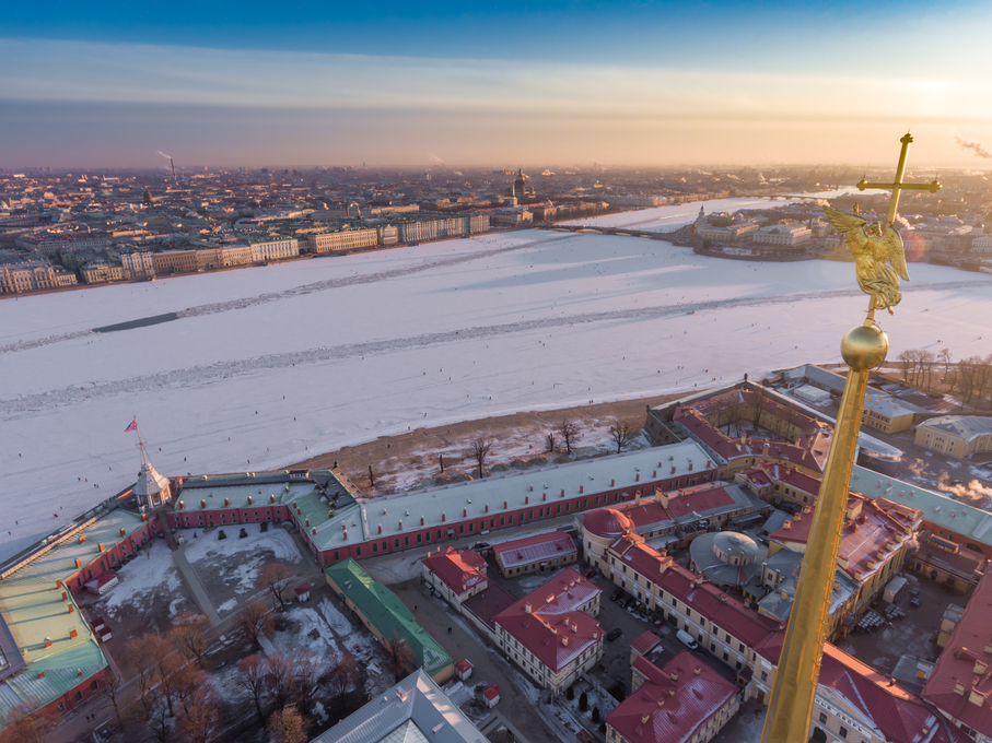 Aerial view of golden Angel and Cross on spike of the Peter and Paul cathedral in Saint Petersburg at sunset, frozen Neva River, sunny frosty day, Winter Palace, Admiralty, Rostral columns