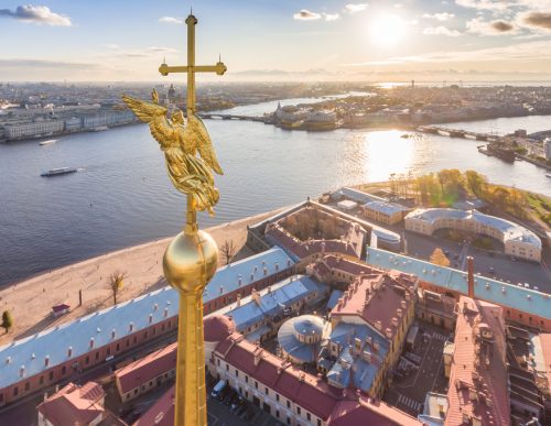 Aerial view of golden Angel and Cross on spike of the Peter and Paul cathedral in Saint Petersburg at sunset, frozen Neva River, sunny frosty day, Winter Palace, Admiralty, Rostral columns