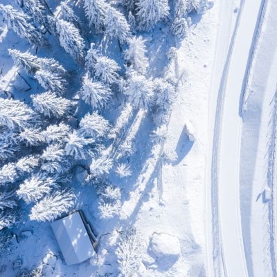 Aerial shot of a forest with trees covered in snow and a two-lane road on the side