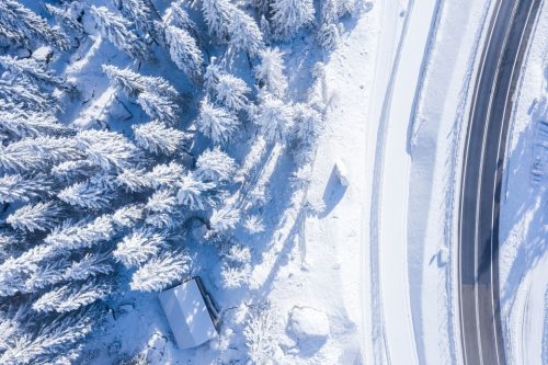 Aerial shot of a forest with trees covered in snow and a two-lane road on the side