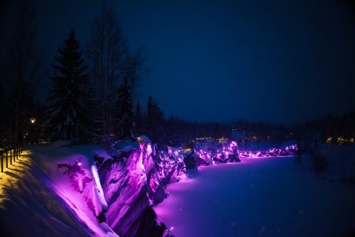 Beautiful panoramic view of night park with colorful lights on winter forest and rocks, Ruskeala, Karelia, Russia