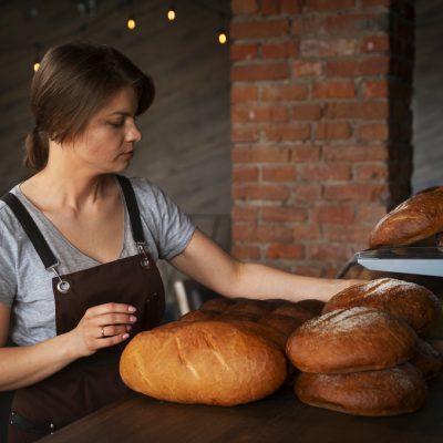female-baker-with-baked-bread-in-the-pastry-shop