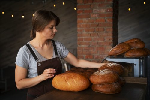 female-baker-with-baked-bread-in-the-pastry-shop